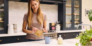 A woman in a kitchen making The Smart Cookie Coffee Bag with a blue mug